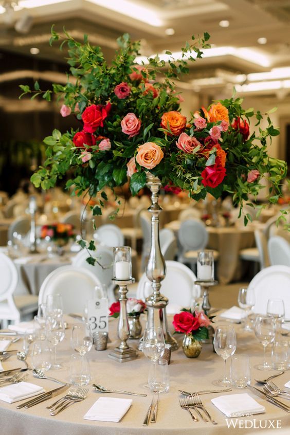 a refined and bright tall wedding centerpiece of peachy, yellow, pink and red blooms and greenery is a stunning idea for a bright wedding