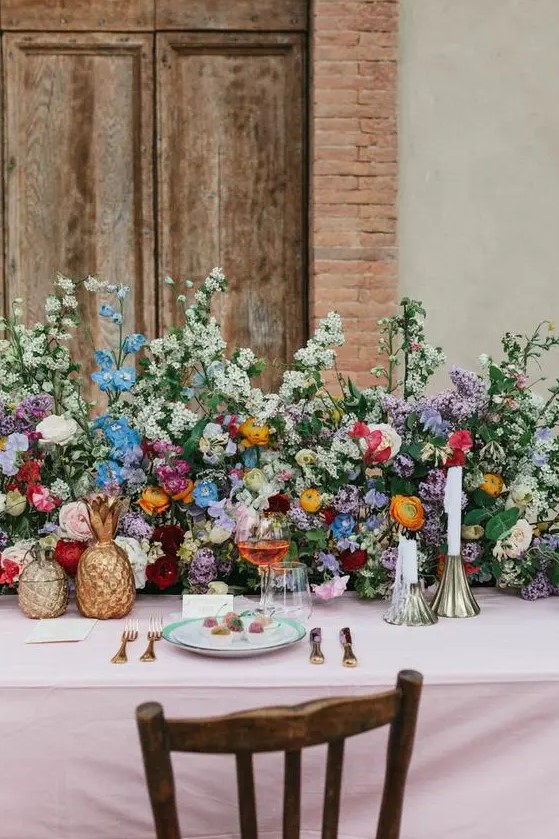 a colorful secret garden wedding table setting with a super lush greenery and bold floral table runner, brass candleholders and gold pineapples