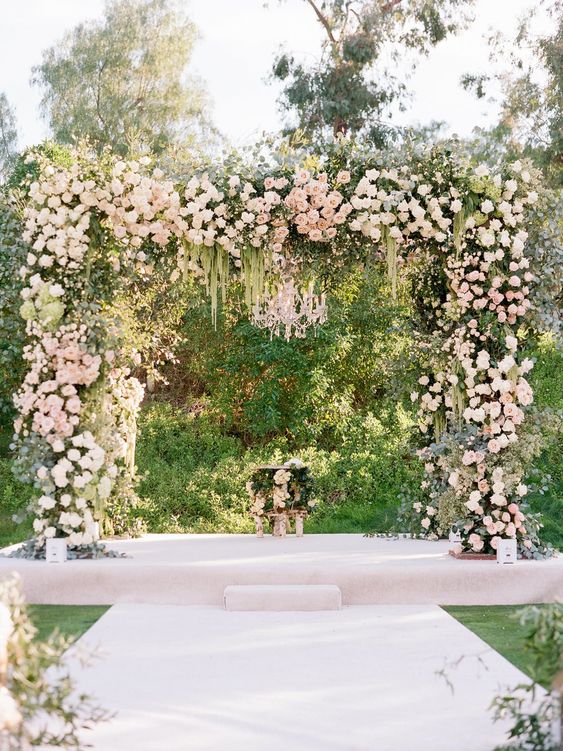 a lush wedding arbor decorated with greenery, neutral and blush blooms and some cascading touches is a lovely idea for a wedding