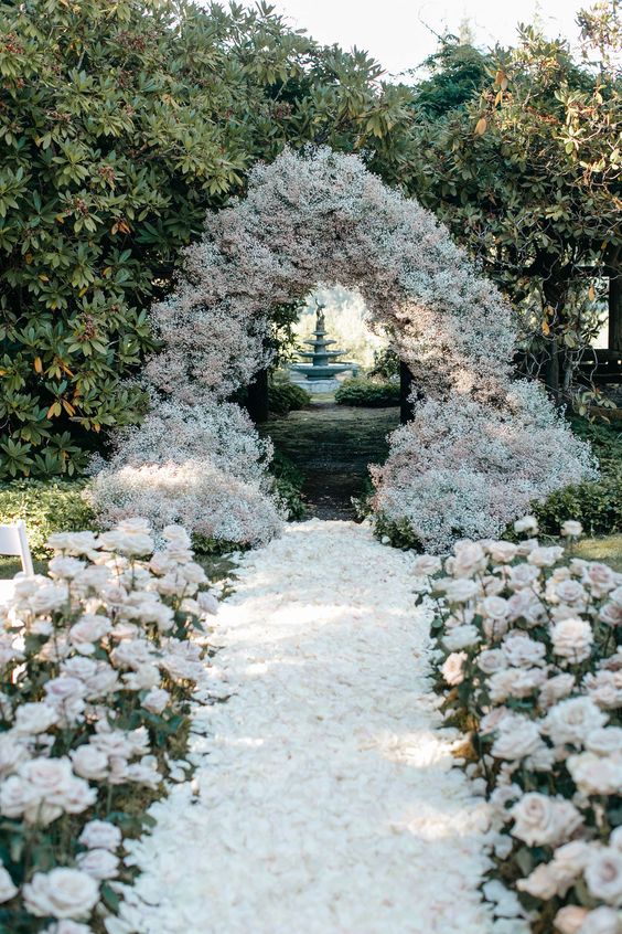 a lush wedding arch composed of baby's breath and with an aisle covered with petals and neutral roses is wow