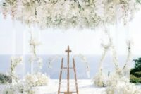 18 a luxurious wedding ceremony space with a sea view, an acrylic arbor with white blooms covering its top and the pillars, pillar candles