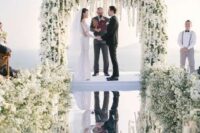 19 a luxurious wedding ceremony space with an incredibly lush white flower wedding arch and matching arrangements on the mirror floor