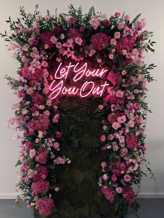 a bright floral wall with light pink and fuchsia blooms and greenery plus a neon sign is a chic and stylish idea