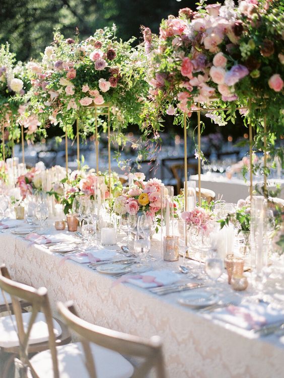 a chic wedding tablescape with pink floral centerpieces and matching tall centerpieces with much greenery and dark and pink blooms