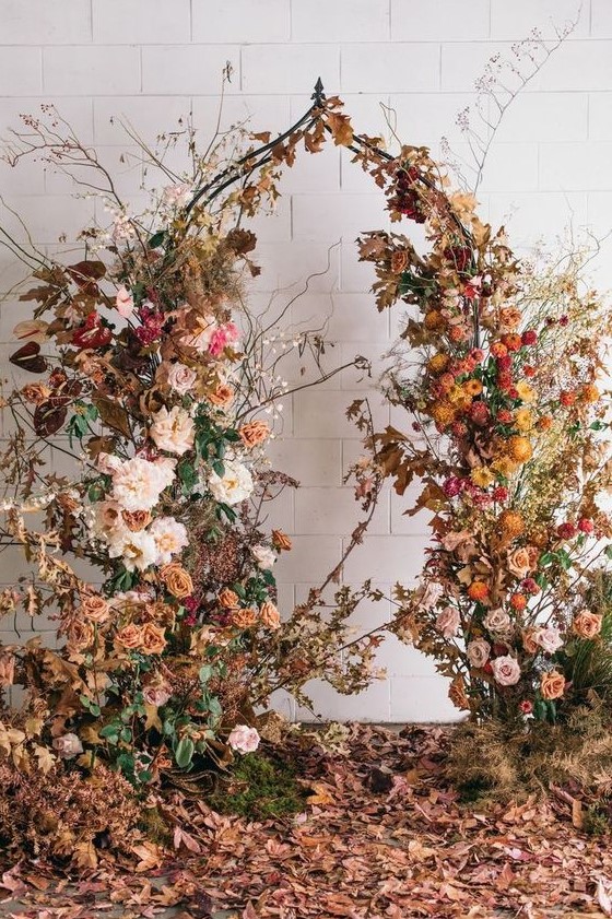 a breathtaking fall wedding arch covered with orange, yellow, blush and pink blooms, dried fall leaves and dried fall branches