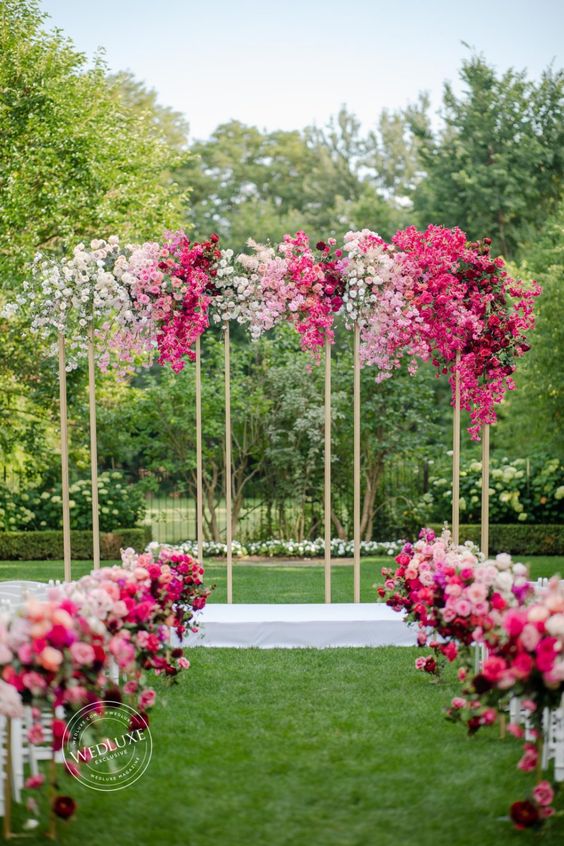 a modern wedding arch with white, light and hot pink blooms creating an ombre effect and matching flowers along the aisle