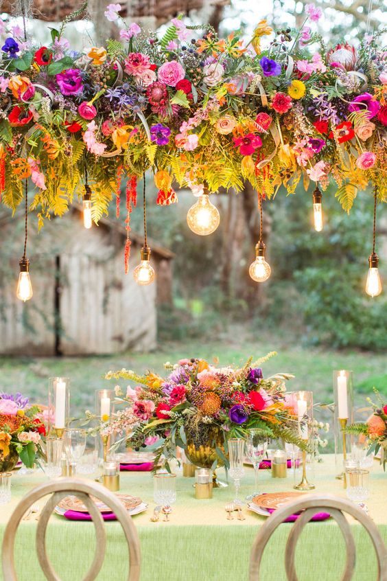 a colorful floral wedding installation of red, pink, purple and orange blooms, greenery and bulbs hanging down
