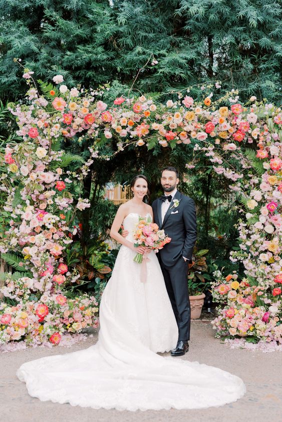 a colorful wedding arch decorated with greenery, blush, coral and pink blooms is a bold idea for a colorful summer wedding