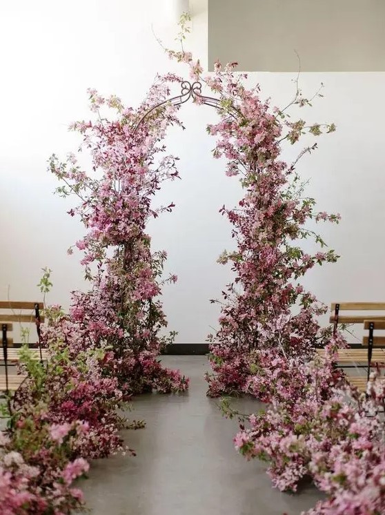 a stunning pink wedding arch decorated with blooming branches and with matching branches lining up the aisle is wow
