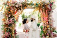 31 a colorful wedding arch with much greenery, bright florals and hanging ribbons and blooming branches for a bold wedding