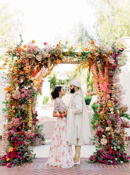 a colorful wedding arch with much greenery, bright florals and hanging ribbons and blooming branches for a bold wedding