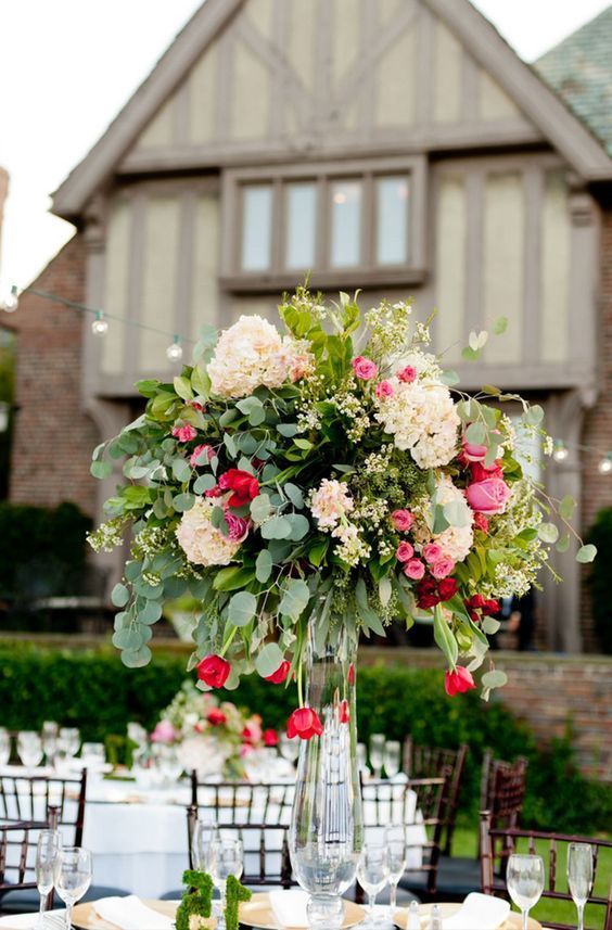 a lush statement wedding centerpiece in a clear vase, with blush, pink and red blooms and greenery is amazing