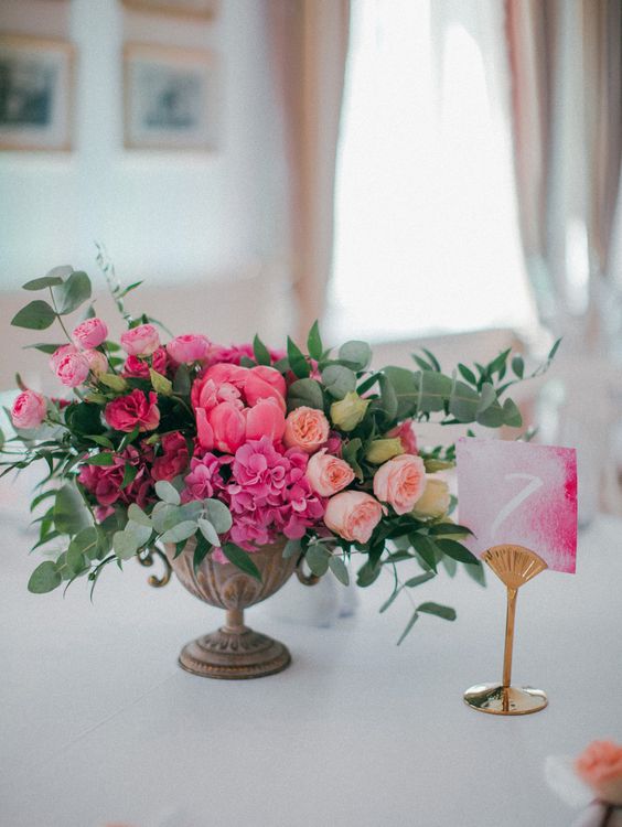 a beautiful wedding centerpiece of blush, hot and bold pink blooms and greenery is chic for a pink wedding