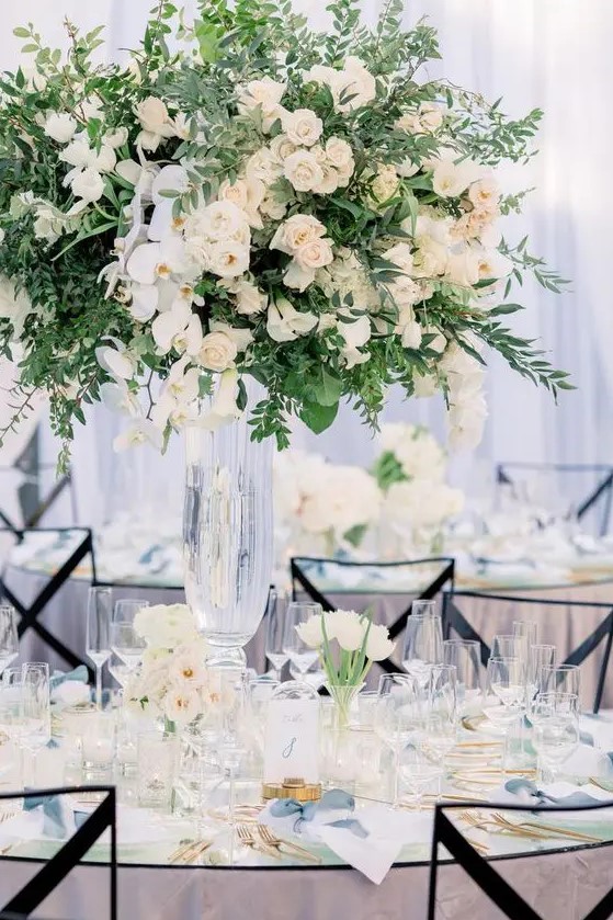 a refined garden wedding centerpiece of much greenery, white roses and orchids is a lush and very beautiful solution