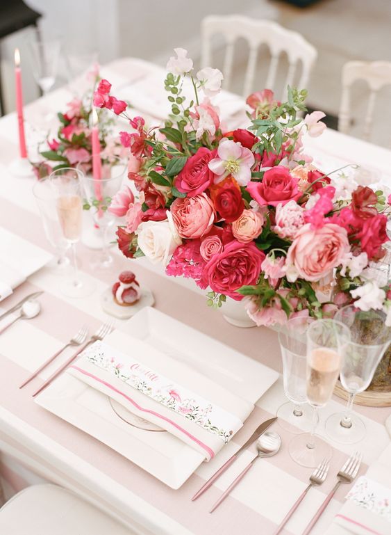 a bold and chic pink wedding centerpiece of light and hot pink blooms, greenery and white flowers plus pink candles