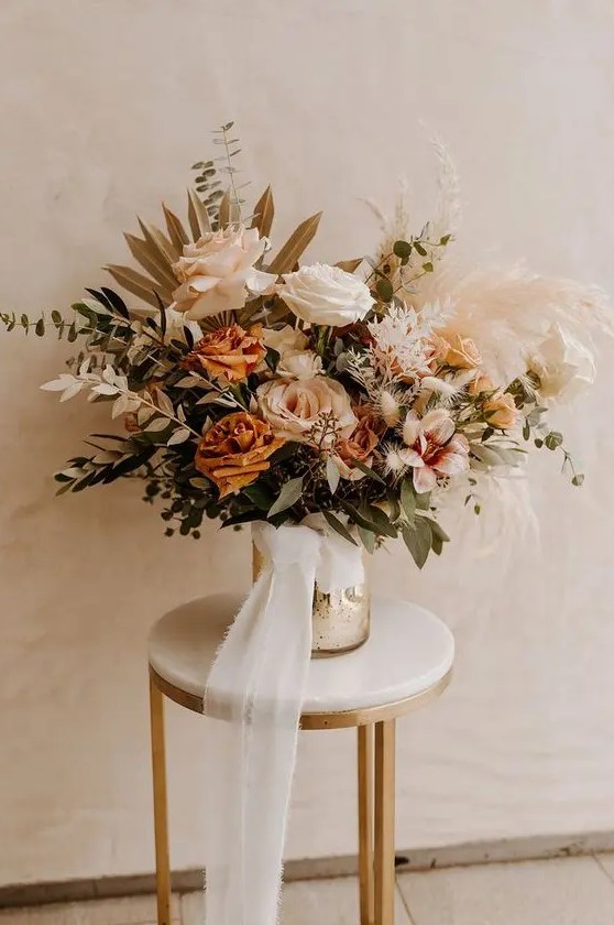 a refined neutral fall boho wedding centerpiece of blush, rust, white blooms, lots of various greenery, pampas grass and dried fronds