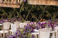 35 a sophisticated wedding reception space with greenery and purple delphinium hanging over the tables and purple blooms and greenery on them