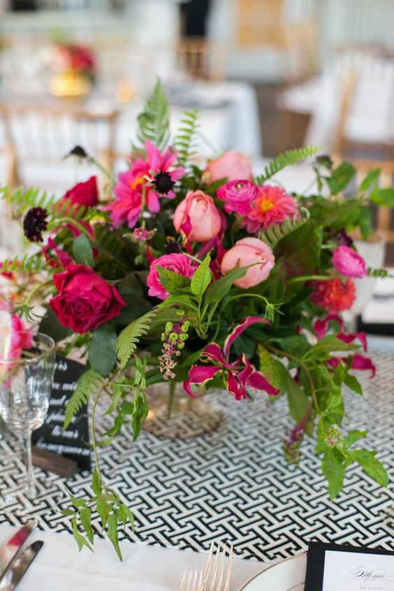 a bright and textural wedding centerpiece of light, hot pink and fuchsia blooms and greenery, berries and deep purple blooms for an accent