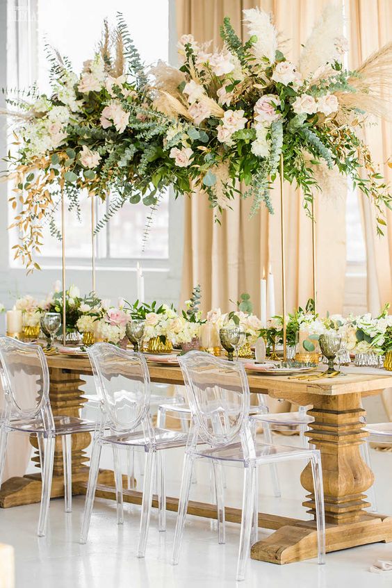 a tall and beautifull wedding centerpiece of greenery, white and blush blooms and pampas grass plsu matching arrangements on the table