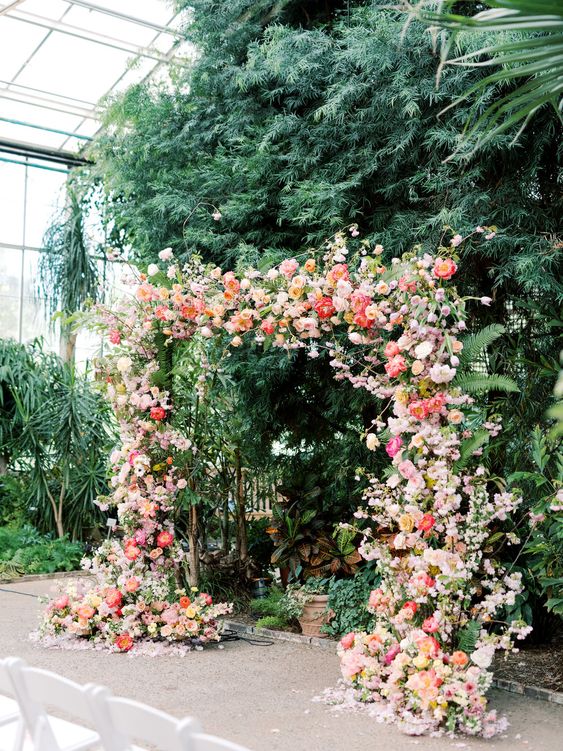 a lush and colorful wedding arch decorated with greenery, blush, coral and pink blooms is a lovely idea for a summer wedding