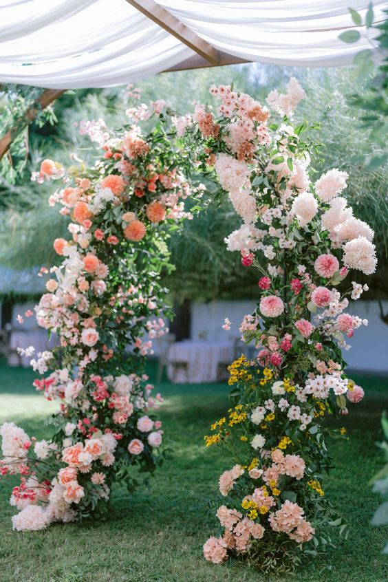 a lush and textural wedding arch decorated with greenery, pink, peachy, blush, orange and mustard blooms is a color statement