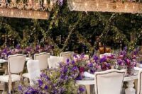 39 a sophisticated wedding reception space with greenery and purple delphinium hanging over the tables and purple blooms and greenery on them