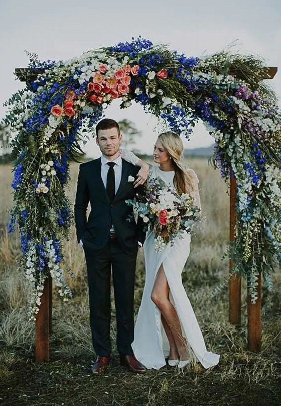 a lush floral arch with peachy roses, white blooms and bold blue flowers on top