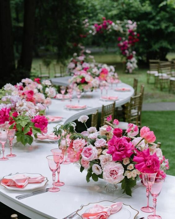 a lively pink wedding centerpiece of light and hot pink blooms, greenery, pink napkins and glasses is amazing