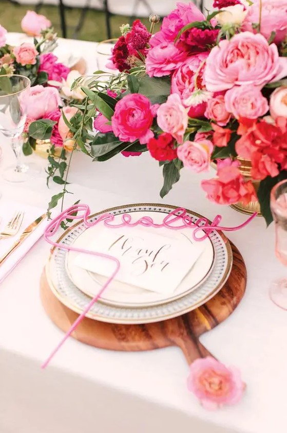 a pretty glam wedding tablescape with light and hot pink blooms, wodoen placemats and pink calligraphy cards, with gold cutlery