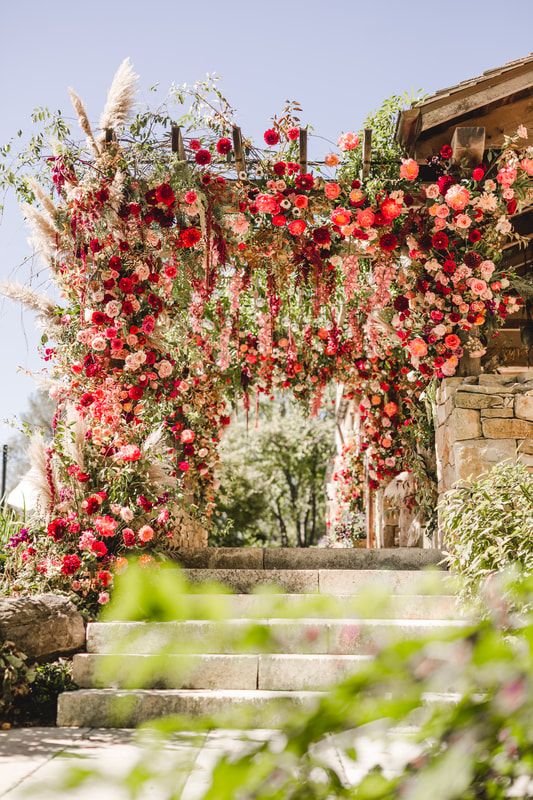 an epic wedding arbor decorated with greenery, pampas grass, pink, red and burgundy blooms is a stunning color statement