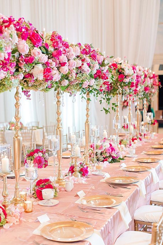 an elegant and sophisticated tall wedding centerpiece of light and hot pink blooms nd greenery plus matching arrangements on the table