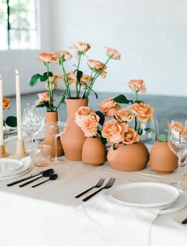a lovely summer or fall wedding centerpiece of terracotta vases and rust-colored roses plus blush candles is chic