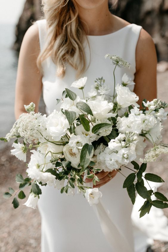 a beautiful all-white wedding bouquet with lisianthus, campanula, lace flower, clematis, spirea, cosmos sister honey