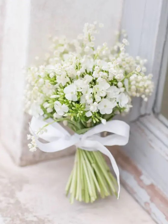 a beautiful and romantic white wedding bouquet of lily of the valley and large blooms with a ribbon bow is amazing