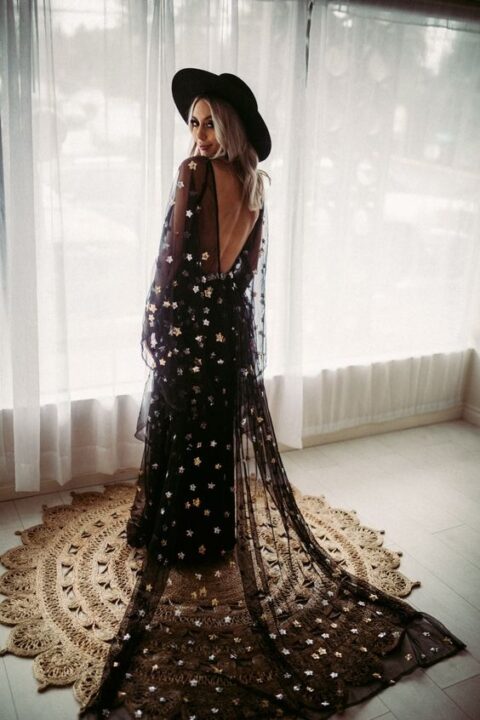 a black and gold star A line wedding dress with illusion sleeves, an open back, a matching cape veil and a black hat