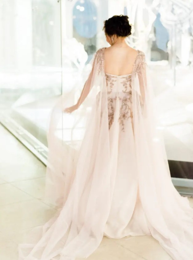 a blush wedding dress with embroidery and beading and a matching cape veil for a chic look