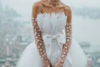 a bold bridal look with a strapless A-line mini dress with a bow, sheer floral long gloves and a pearl necklace