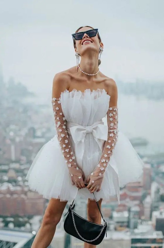 a bold bridal look with a strapless A line mini dress with a bow, sheer floral long gloves and a pearl necklace