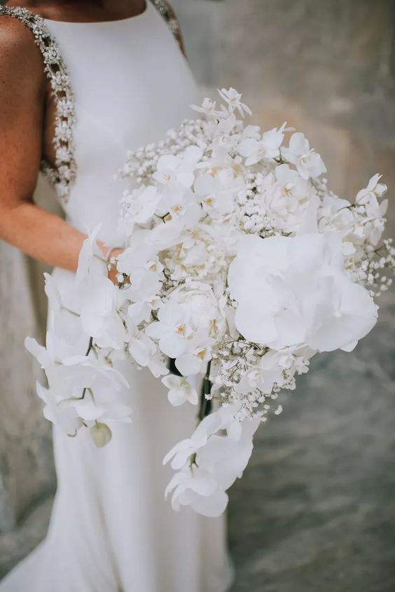 a cascading white wedding bouquet of orchids and baby's breath is a beautiful and fresh solution for a sophisticated bride