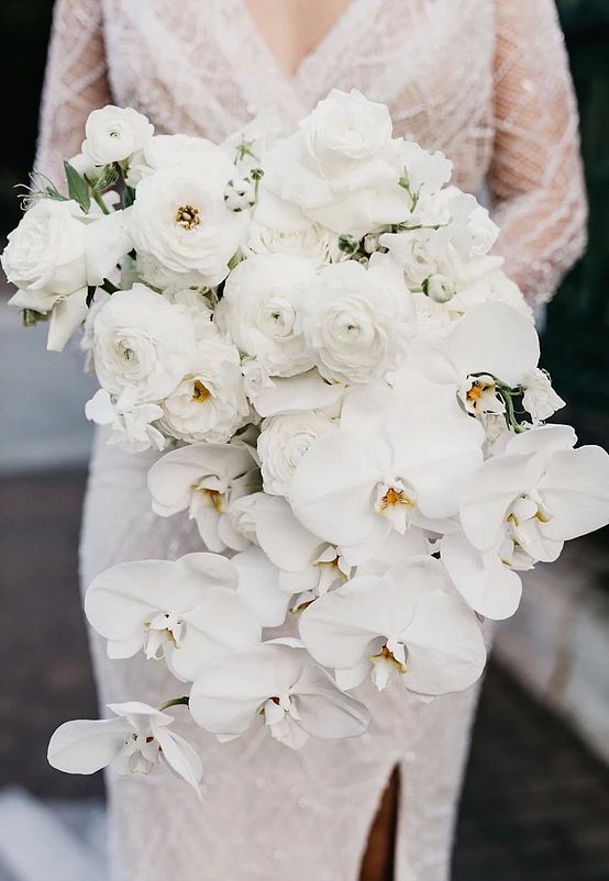 a cascading white wedding bouquet of ranunculus and orchids is a beautiful idea for a modern wedding