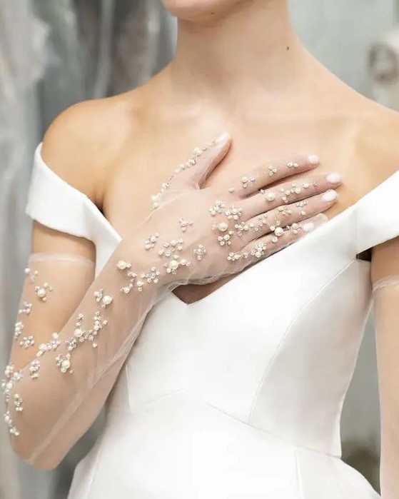 a chic modern wedding dress with a deep neckline and sheer long gloves with pearls and rhinestones are a lovely combo