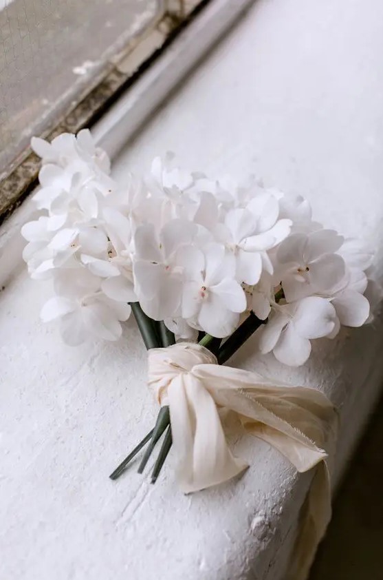 a chic one flower wedding bouquet in white, with neutral ribbons is a lovely idea for a minimalist and refined wedding