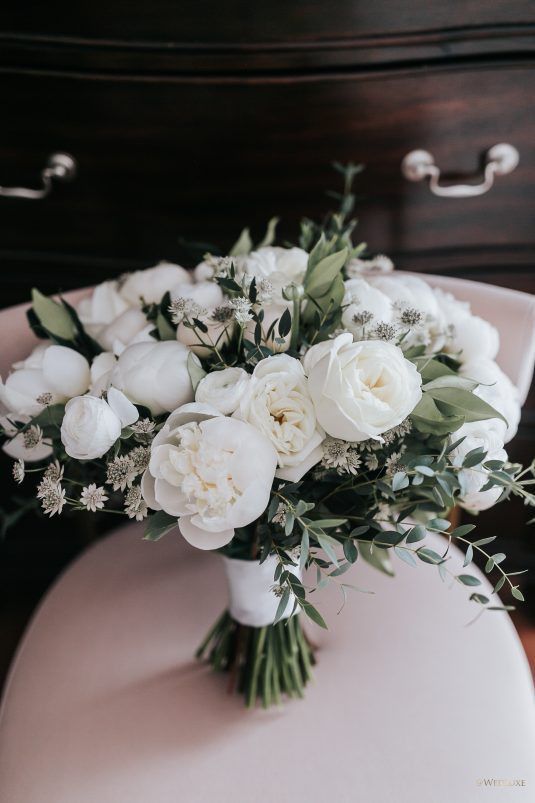 a classy all-white wedding bouquet of peony roses, peonies, some white fillers and greenery is a fresh summer idea