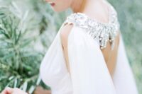 a draped wedding dress paired with a matching capelet with a heavily embellished shoulder detail