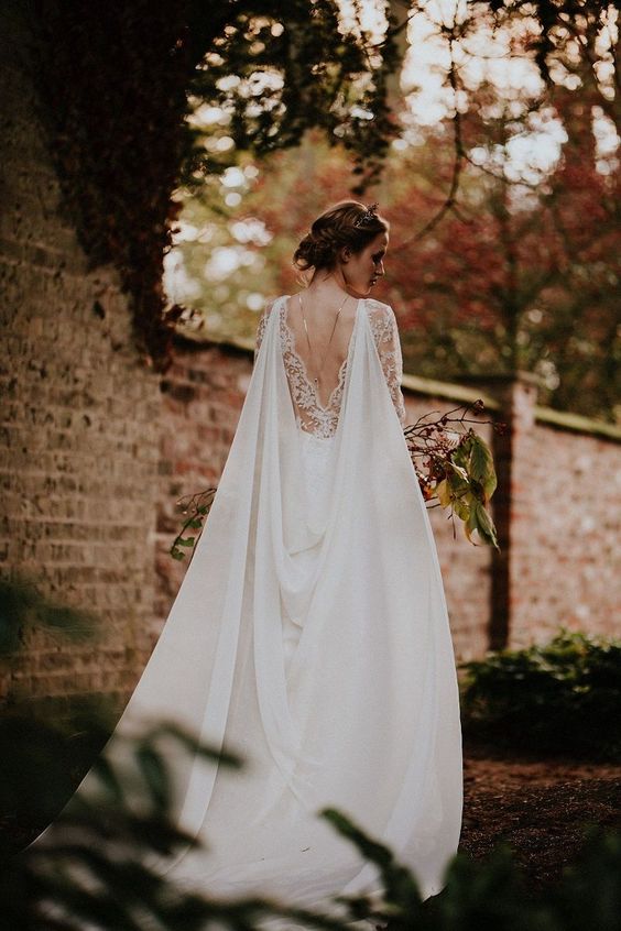 a lace wedding dress with a cutout back, a back necklace and a bridal cape veil is really regal and stunning