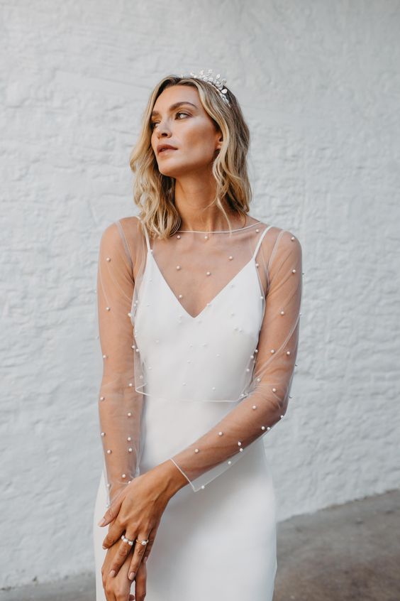 a minimalist slip wedding dress with a sheer pearl dress topper with long sleeves and a crystal crown are a lovely combo