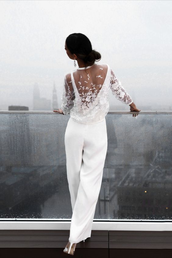 a minimalist white jumpsuit paired with a sheer lace applique topper with long sleeves and heels creates with a chic modern bridal look