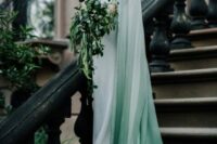 a modern enchanted forest bridal look with a minimalist off the shoulder dress and an ombre white to green capelet with a train is wow