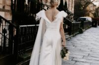 a modern silk bridal jumpsuit with a cutout back and a sheer cape veil with large bows on the shoulders are a bold combo