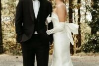 a modern sophisticated bridal look with a strapless plain wedding dress with a big bow on the back and matching long gloves plus pearl earrings